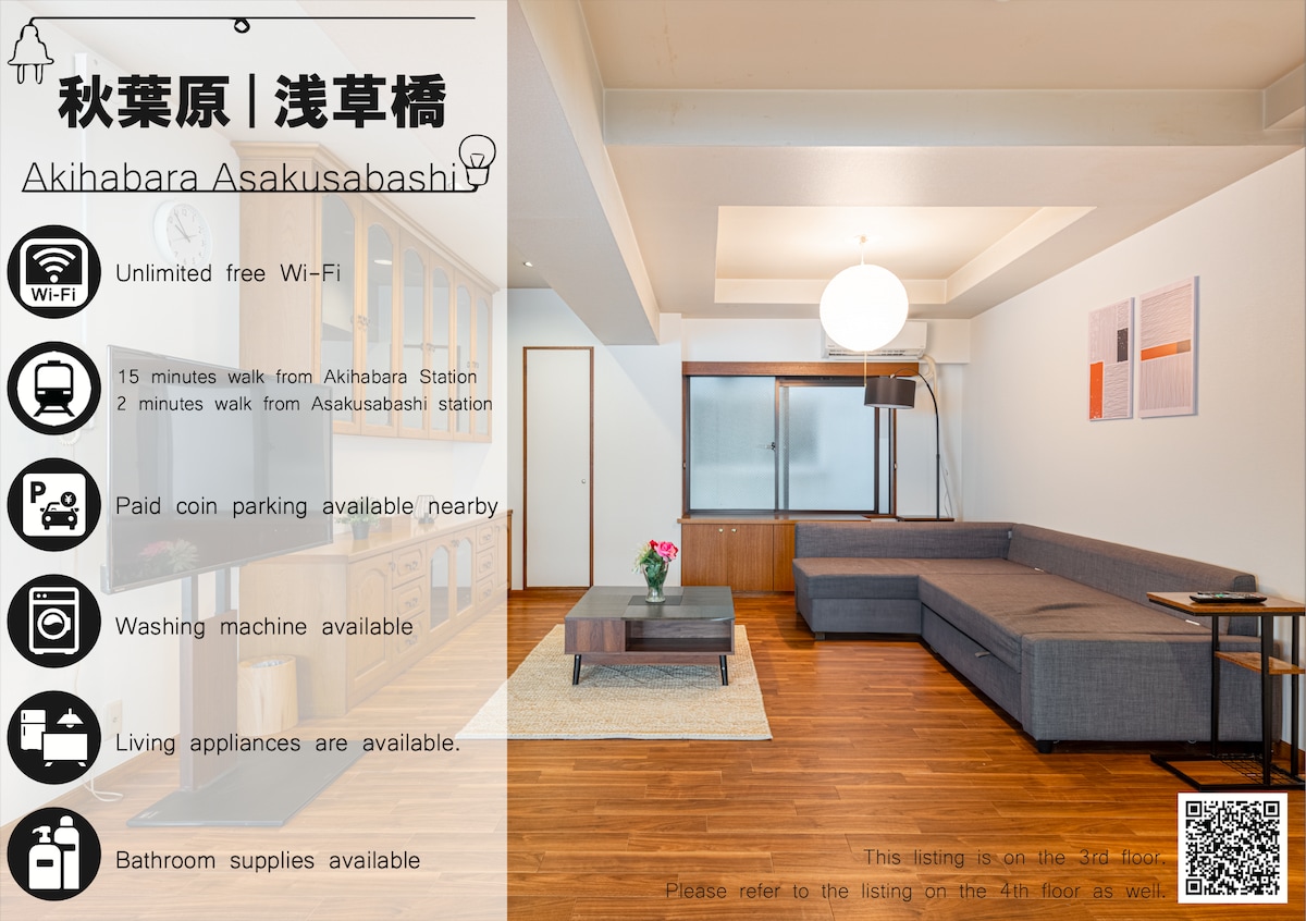 A spacious living room features a double-sized sofa bed, wooden flooring, and a round ceiling light. Minimalist furniture creates an open atmosphere, while a large window allows natural light to fill the space, adding brightness.