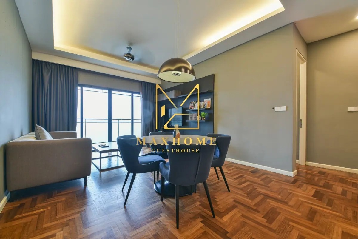 A contemporary living space features a round dining table with four chairs, surrounded by stylish decor. A comfortable sofa is positioned nearby, with large windows allowing natural light to brighten the room. The warm wooden flooring complements the modern furnishings.