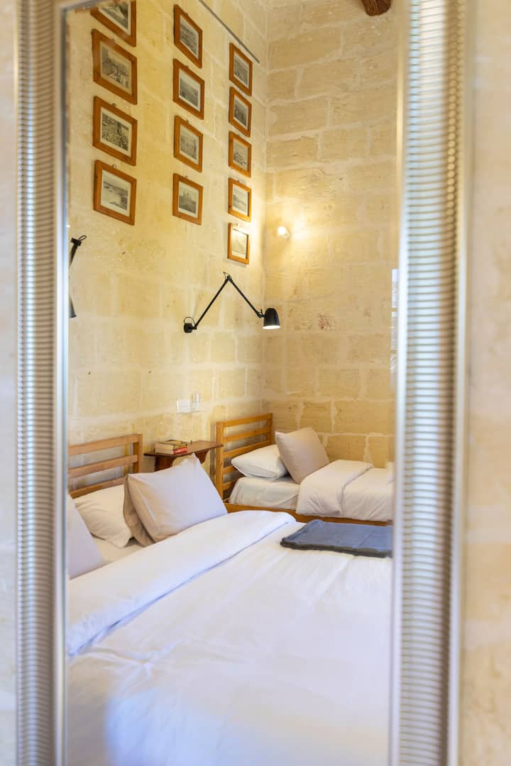 חדר שינה נוח ומרווח לשלושה בחווה Ta' Nikola, עם עיצוב כפרי מסורתי, מצעים נעימים ואור טבעי רך - מושלם לשהייה מרגיעה עם בני משפחה או חברים בסביבה אותנטית של גוזו