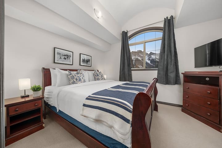 Уютна спалня със зашеметяваща гледка към планината, оформена от елегантен сводест прозорец, идеална за почивка след приключенски ден.