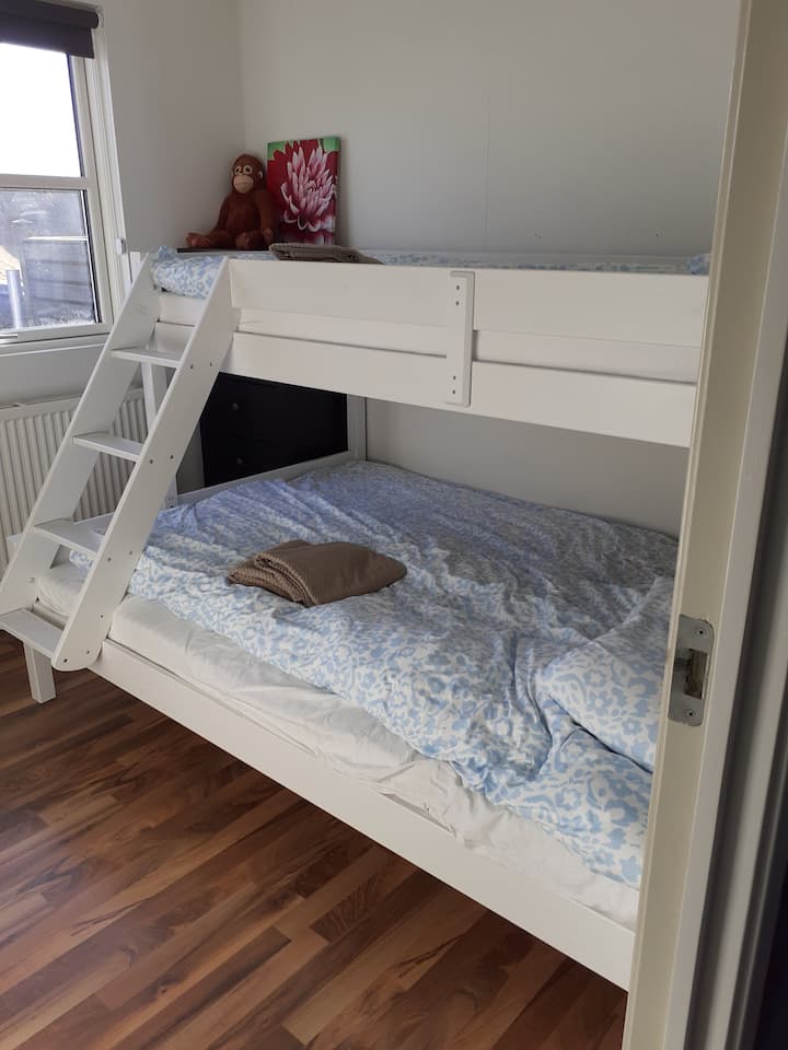 The family room with double bed below and a bed on top. Chest of drawers, chair and table in the room as well