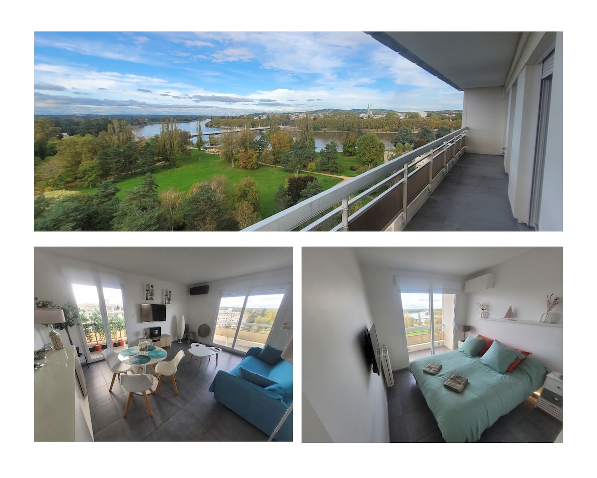 A panoramic view reveals a serene landscape featuring lush greenery and a waterway, seen from a spacious balcony. The interior showcases a bright, comfortable living area with a cozy sofa, dining table, and wall-mounted TV. A tranquil sleeping space includes a spacious bed, accentuated by soft linens.