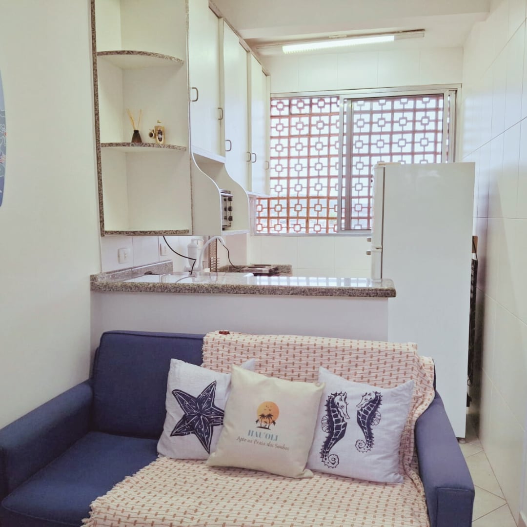 A compact kitchen area features a white refrigerator and granite countertops. A navy blue couch, adorned with decorative cushions, provides a cozy seating option. Natural light filters through a decorative window, enhancing the bright ambiance of the space.