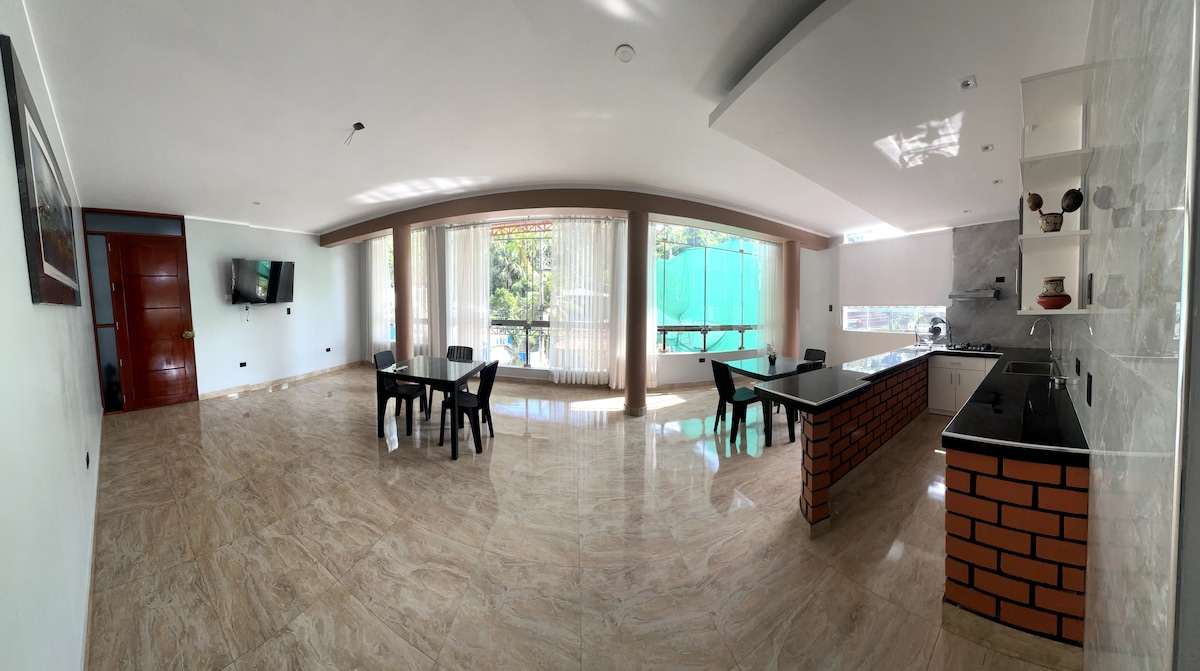 A spacious living area is defined by large windows allowing natural light to fill the space. The kitchen features sleek countertops and ample cabinetry. A dining table is placed beside the kitchen, while a comfortable seating area is arranged for relaxation.
