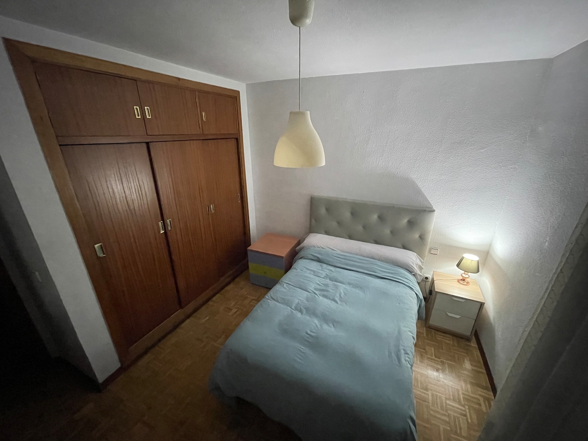 A peaceful sleeping area is furnished with a spacious bed covered in a light blue duvet. A small nightstand with a lamp is positioned beside the bed, while a built-in wardrobe provides storage. Soft lighting enhances the calming ambiance of the room.
