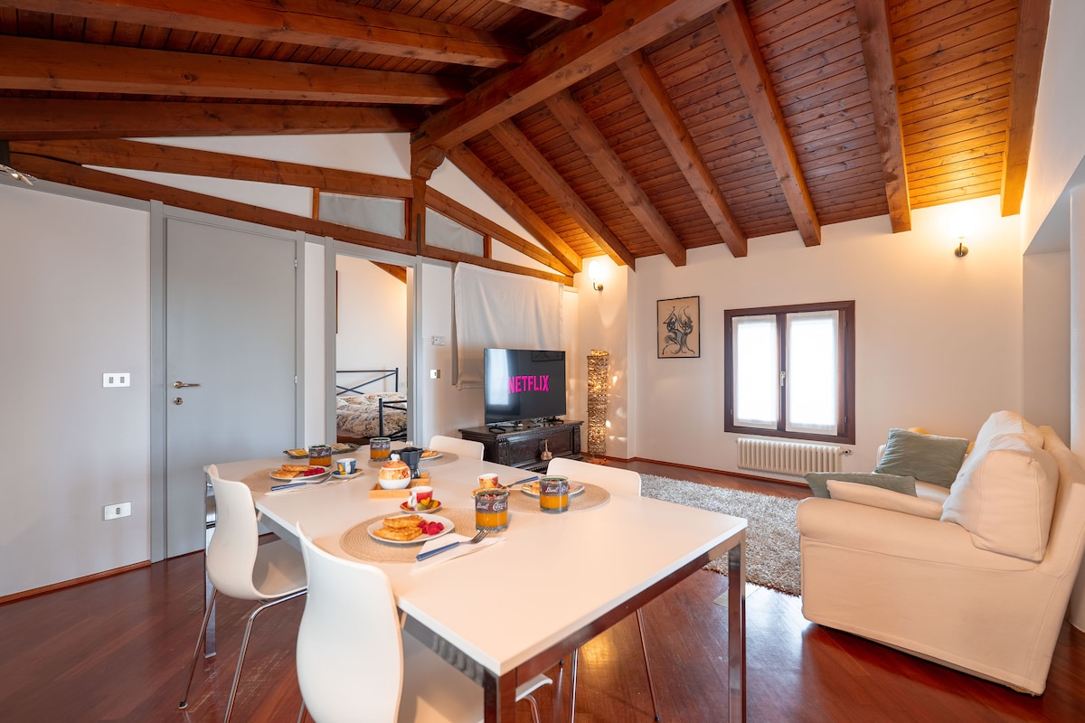 Gemütliches Wohnzimmer mit sichtbaren Holzbalken: Enthält ein gemütliches Sofa, einen 55-Zoll-Smart-TV, der sich perfekt für entspannte Abende eignet, und einem weichen Teppich, der Wärme spendet. Mehrere Kakteen vervollständigen das Design.