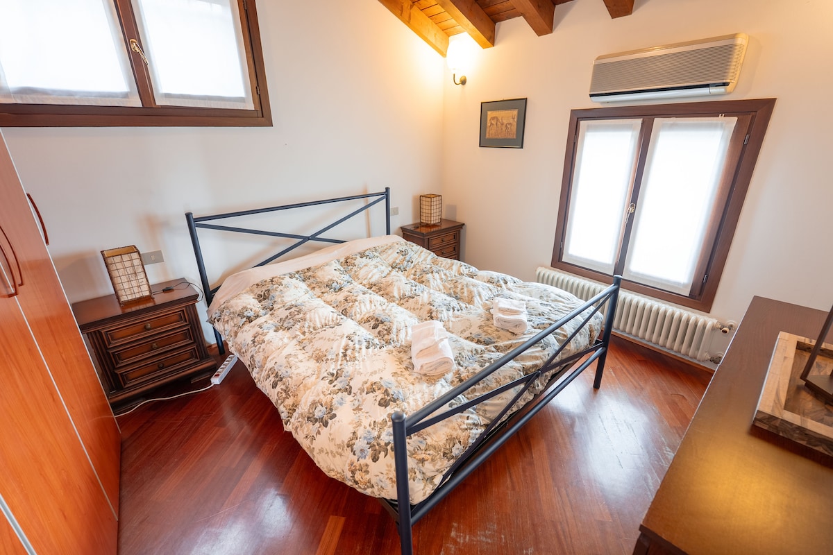 Helles Doppelzimmer mit Sichtbalken und Parkettboden. Ausgestattet mit einem schmiedeeisernen Bett, Nachttischen mit Designerbajour und großem Kleiderschrank. Die Fenster empfangen reichlich natürliches Licht und machen die Umgebung intim und einladend.
