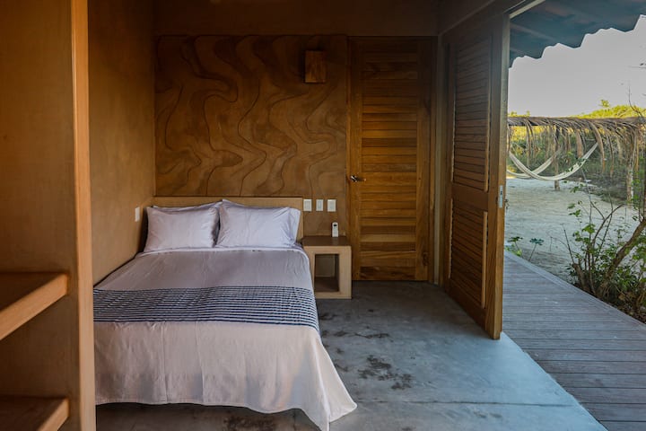 E rrethuar me çimento të gdhendur dhe dru të ngrohtë, kjo dhomë dopio "queen" hapet për hamakë, dritë dhe qetësi të butë të kopshtit.