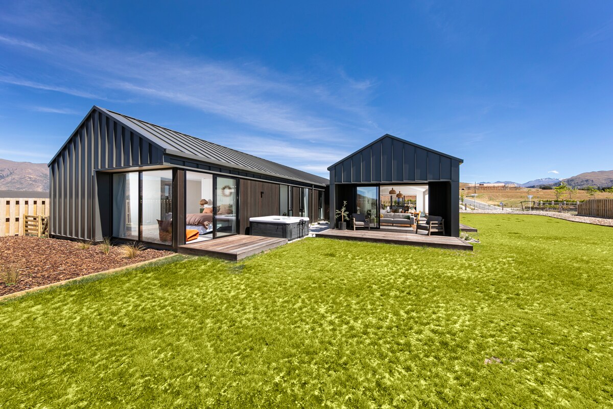 A modern family home is set in a spacious yard with a well-maintained lawn. Large glass doors provide access to outdoor areas, showcasing views of the surrounding landscape. A spa pool is featured on a wooden deck, enhancing the outdoor entertaining space.