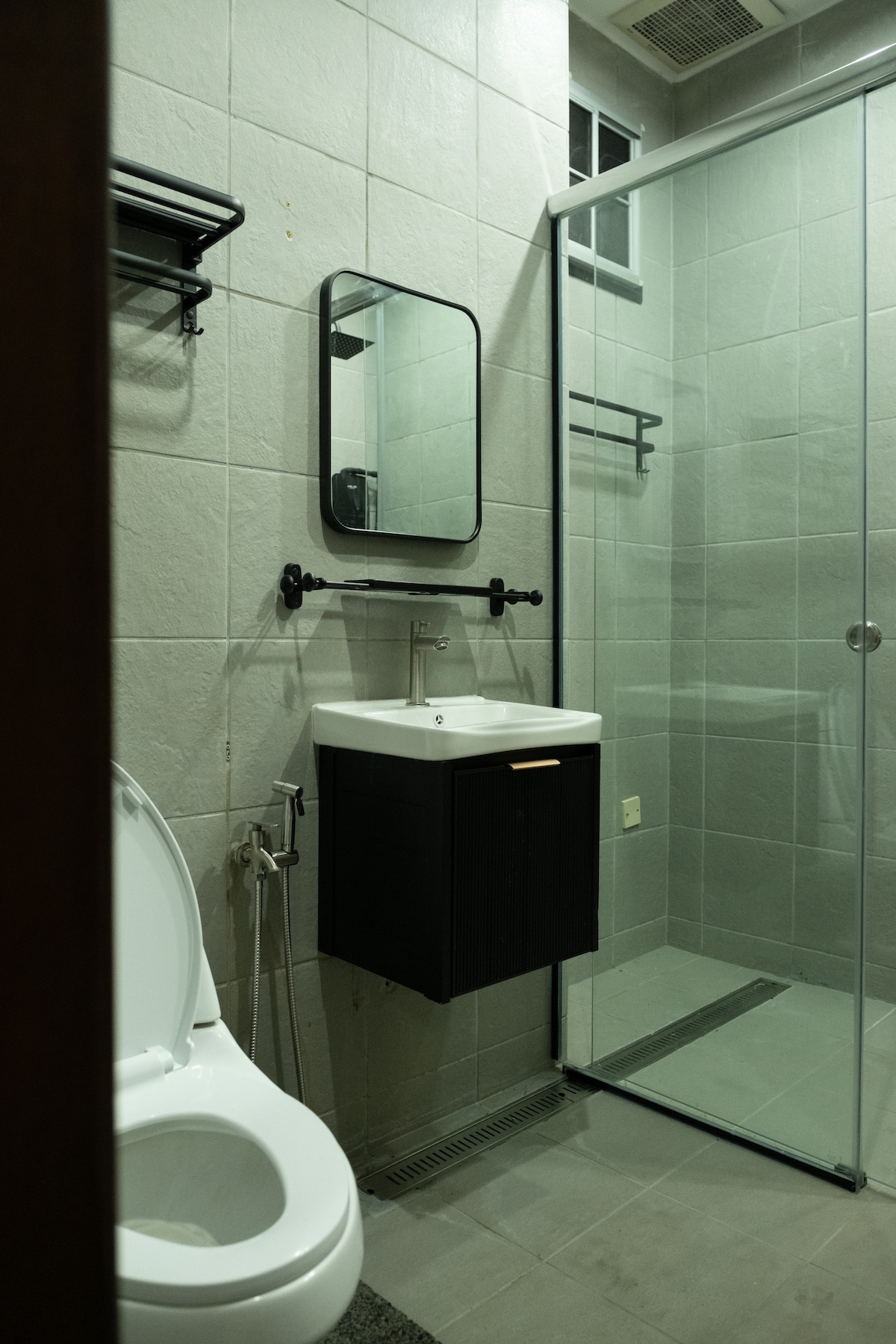 A modern bathroom features a sleek glass shower enclosure with a black and white color scheme. A wall-mounted mirror reflects the space, while a compact vanity with a single basin is positioned beneath it. The toilet is discreetly placed near the corner.