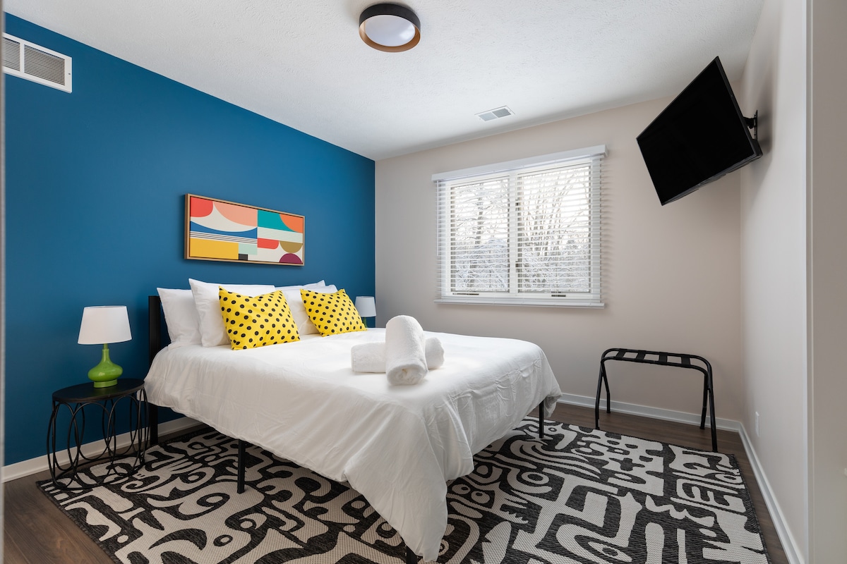 "Bedroom 9 is full of personality with a cozy queen bed, playful yellow polka dot pillows, and colorful artwork. The vibrant accent wall adds charm, while the 43" TV and convenient luggage racks enhance your comfort and convenience."