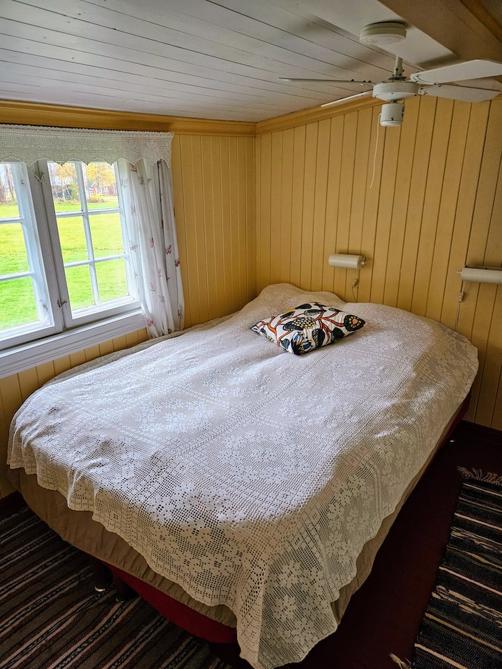De slaapkamer in Unit 1, Seterstuggu. Raam weg van de tuin, richting het veld. De kamer heeft rustgevende gele muren en een heerlijk, zacht 150 bed. Ventilator in het plafond. 
Ladekast voor opslag en kasten met wasapparatuur. 