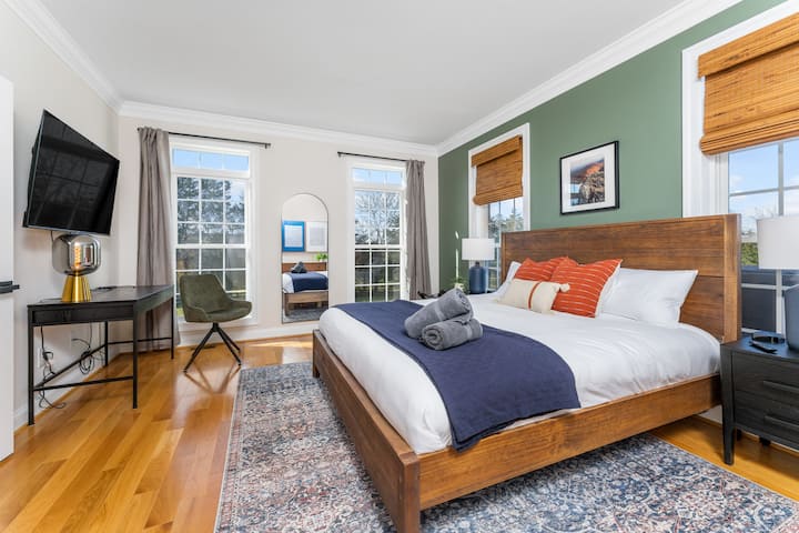 Chumba cha kulala cha ghorofa ya kwanza kilicho na kitanda cha King, televisheni kubwa ya 4K, sehemu mahususi ya kufanyia kazi na mandhari bora ya ua wa nyuma na misitu.