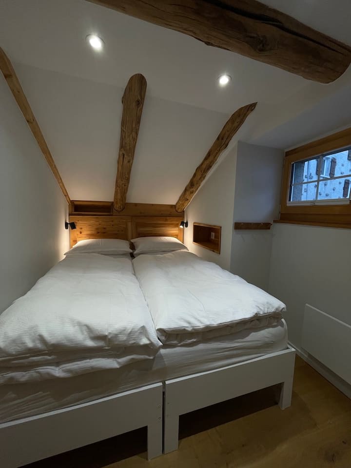 Cette chambre confortable nichée à l'arrière au deuxième étage dispose d'un lit double (160 x 200 cm), d'étagères et de crochets. Parfait pour se reposer après une journée d'aventures à Saas-Fee.