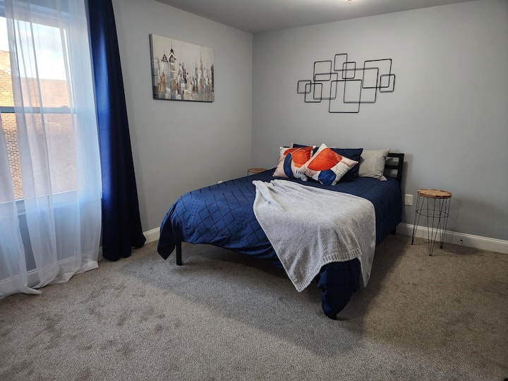 Dormitorio luminoso y acogedor con una cama tamaño queen, ropa de cama vibrante y sábanas suaves. La gran ventana deja entrar la luz natural, mientras que la decoración moderna agrega un toque elegante. Perfecto para relajarse o recargar energías después de un día ajetreado  