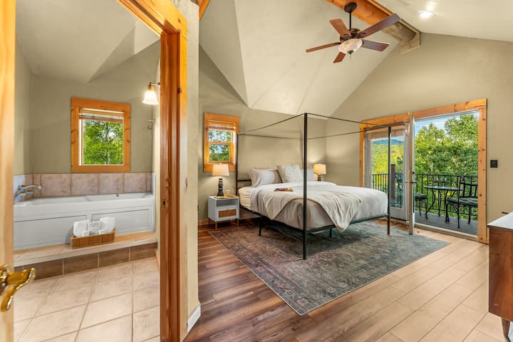 Pokojná hlavná spálňa na poschodí s klenutými stropmi, manželskou posteľou s baldachýnom a výhľadom na stromy a kopce z vlastného balkóna. Útulné, čisté a navrhnuté na hlboký odpočinok.