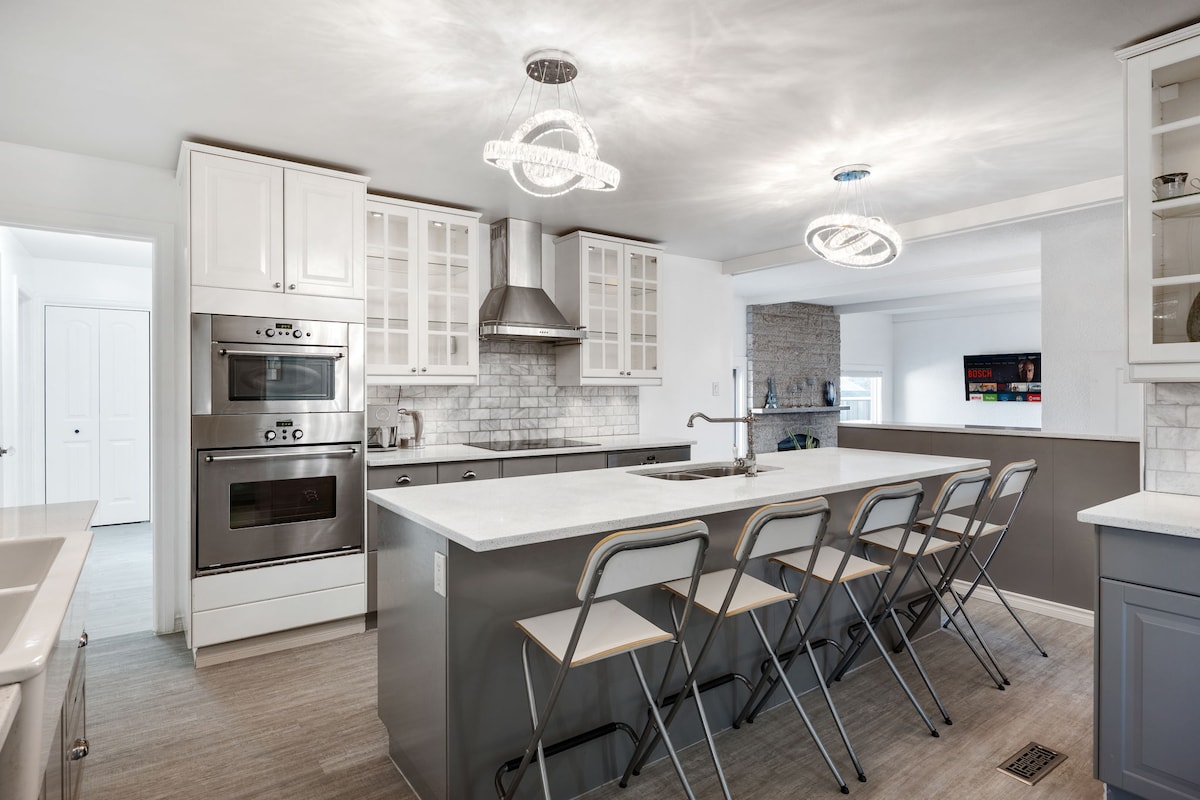 The kitchen showcases a modern design with a large island featuring seating for several. Stainless steel appliances and cabinetry with glass accents enhance the space. Soft lighting fixtures add warmth, while the open layout connects to the adjacent living area.