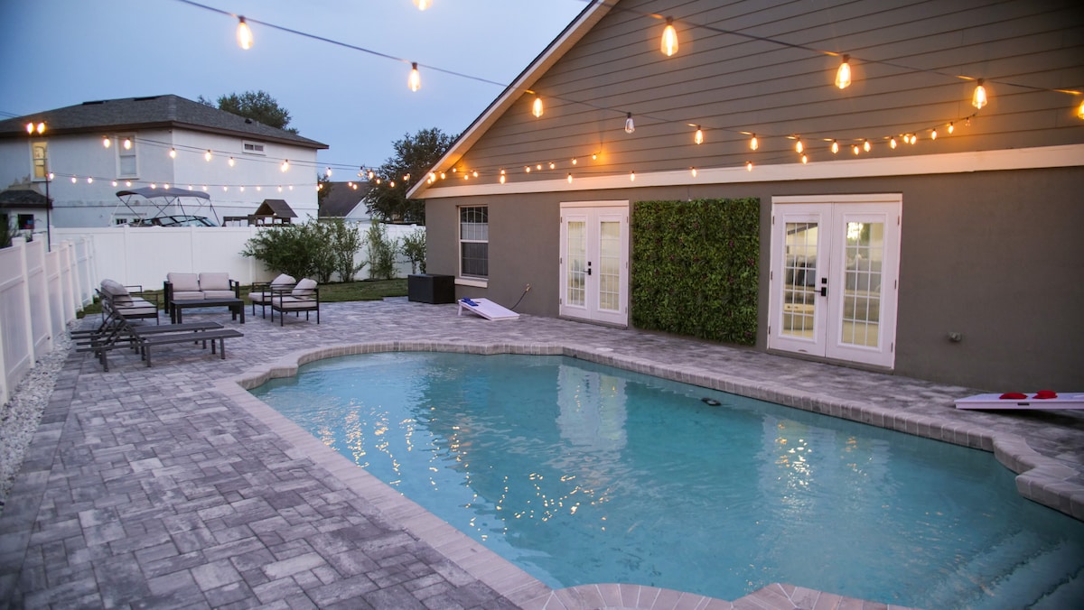 A private pool area is featured, surrounded by smooth stone flooring and illuminated by string lights. Comfortable lounge chairs are arranged nearby, inviting relaxation. The pool's clear water reflects soft evening light, enhancing the serene ambiance of the space. Lush greenery adorns the wall, contributing to the tranquil atmosphere.
