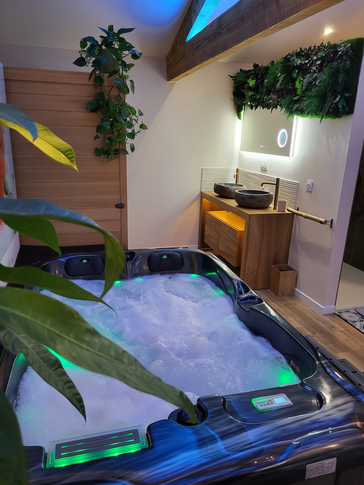 A private hot tub is set against a soothing backdrop of greenery, featuring colorful LED lighting. The area is complemented by natural wood accents and a sleek vanity, inviting relaxation in a tranquil environment.