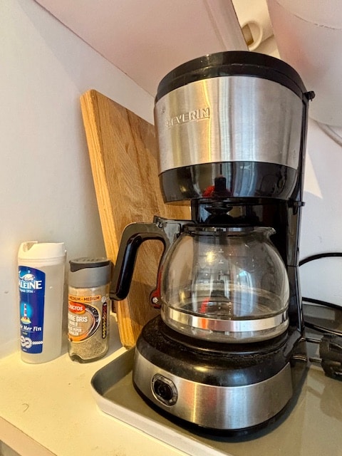 A coffee maker is displayed on a countertop, featuring a glass carafe and stainless steel accents. Nearby, a bottle of creamer and a container of spices are visible, adding to the kitchen's functionality.