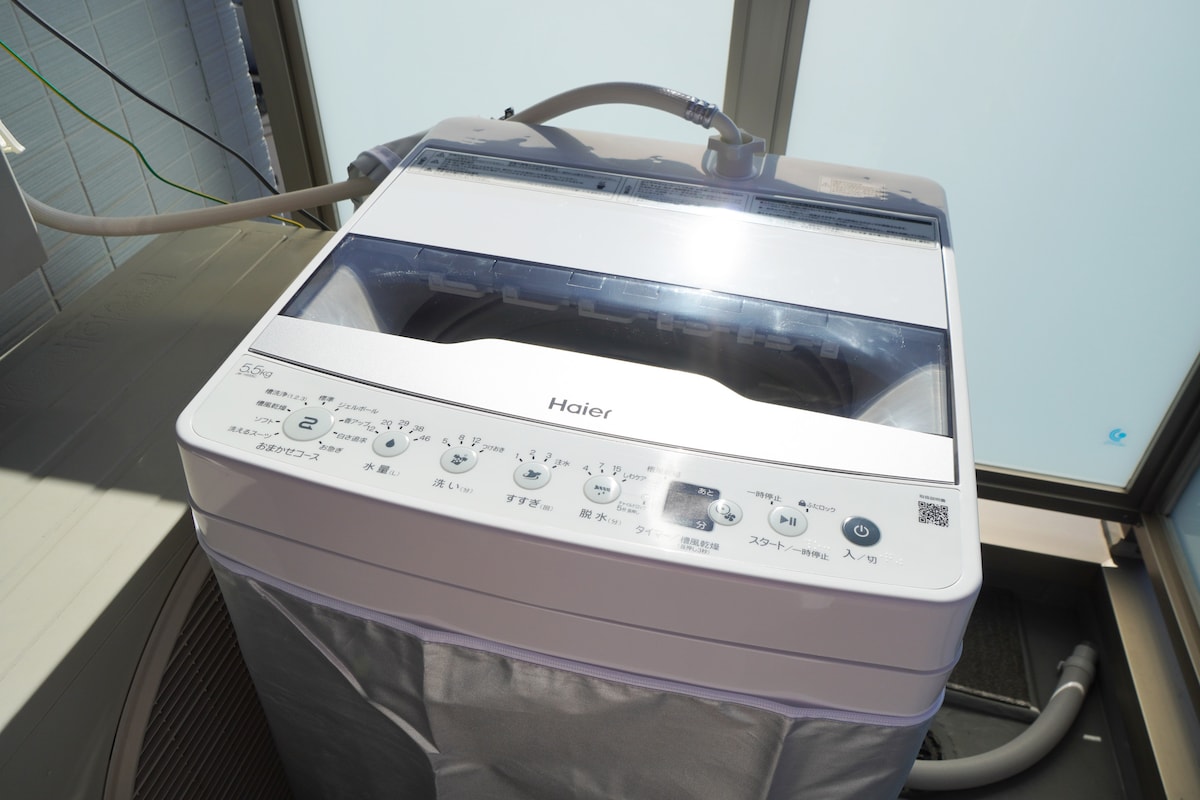 A compact washing machine is displayed with controls visible on the top panel. The machine is positioned near a window, allowing for natural light to illuminate its white exterior.