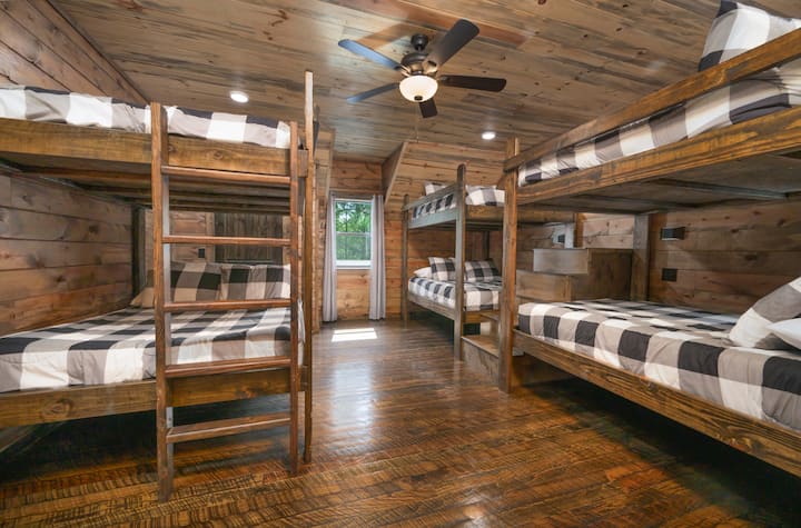 Rustic cabin bunk room with a full-size bed, warm wood interiors, checkered bedding, and cozy lodge vibes.