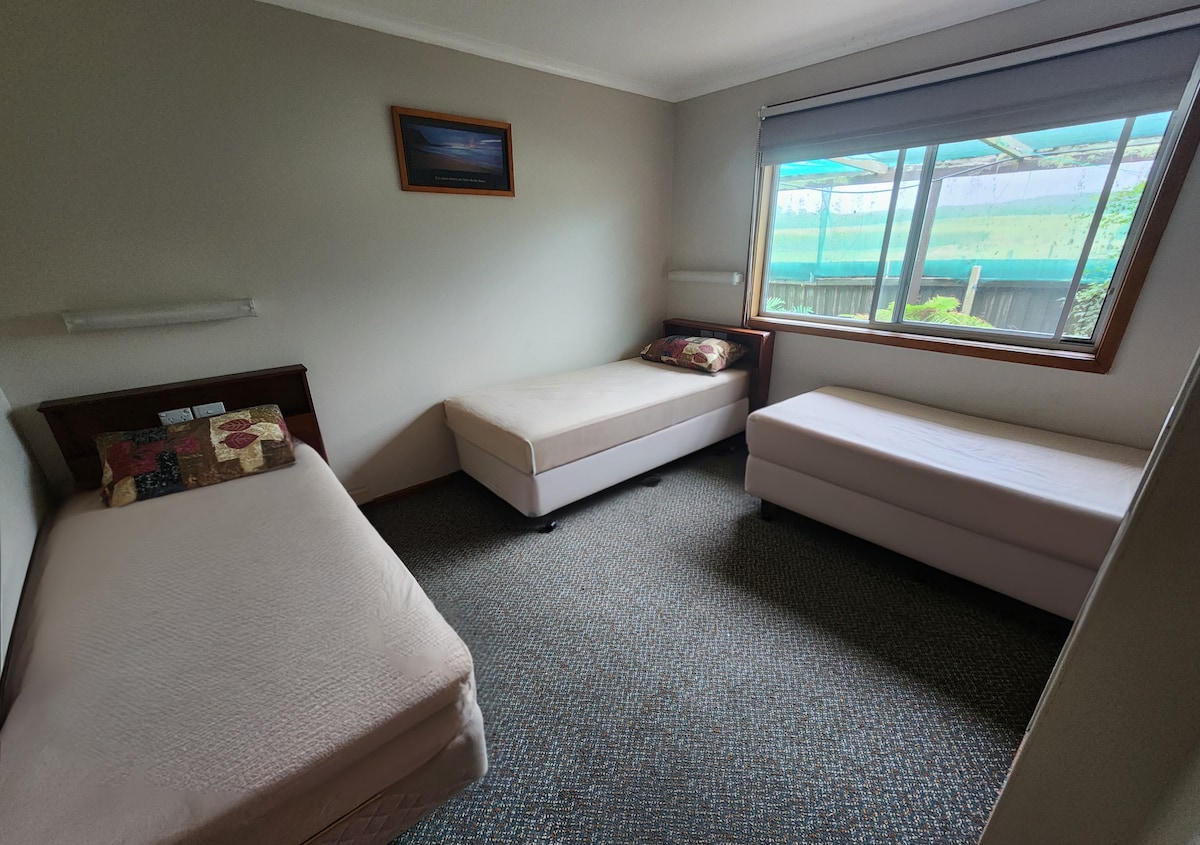 寝室2 - シングルベッド3台、下部寝具、枕、蛍光灯のベッド照明、遮光カーテン、カーペットの床。