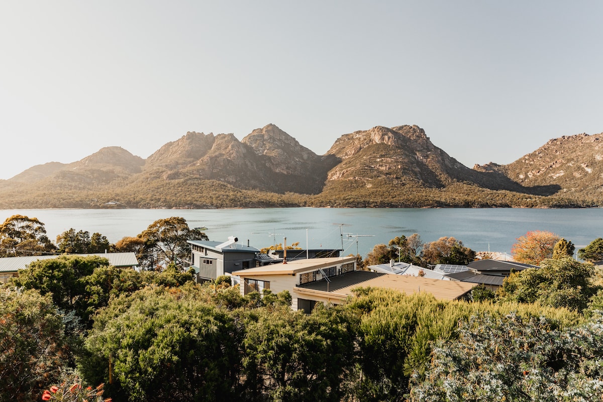 A panoramic view captures the serene landscape, showcasing the sweeping Great Oyster Bay framed by the majestic Hazard Mountains. The foreground features lush greenery, highlighting the natural beauty surrounding the property.