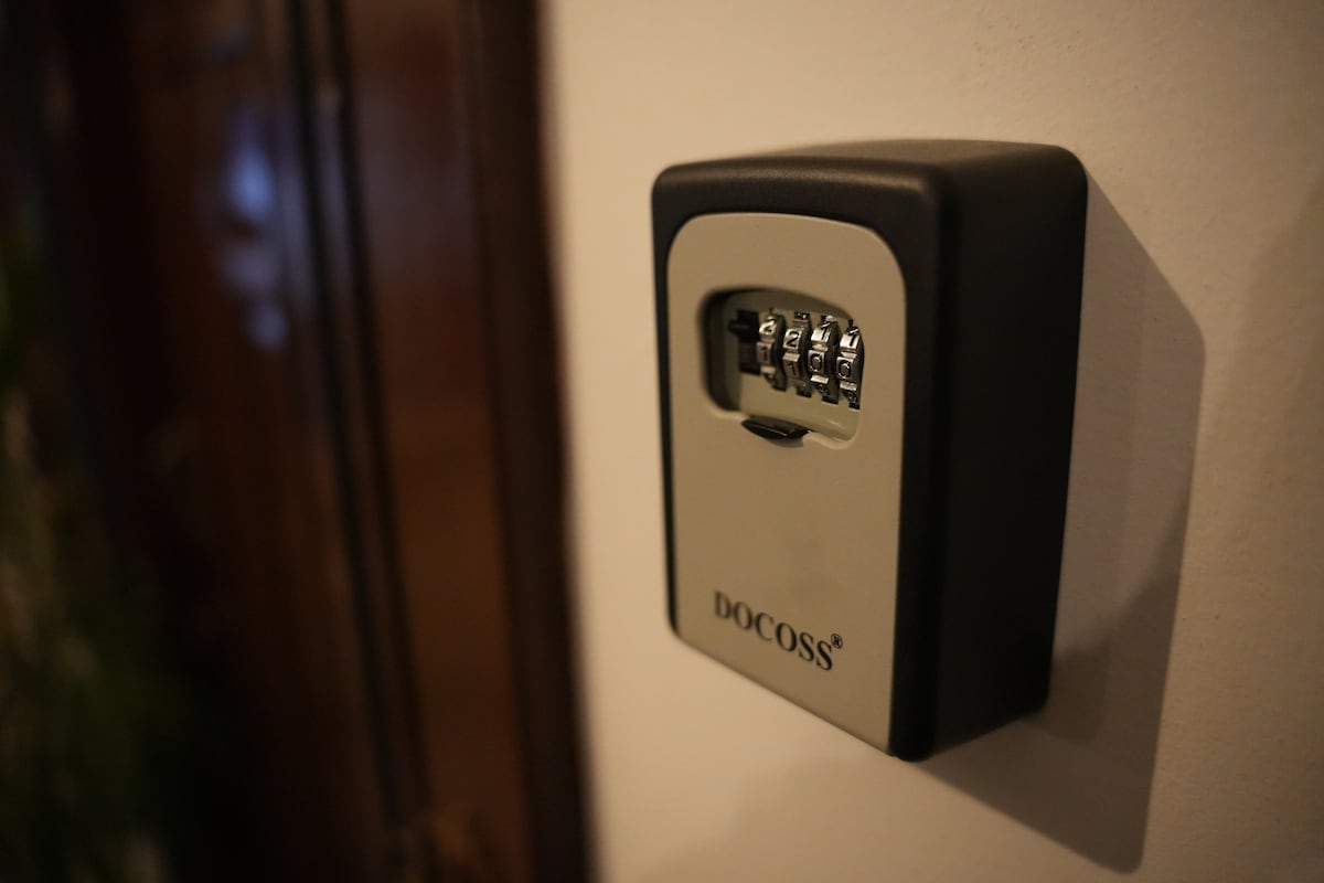 A secure wall-mounted combination lock box is displayed, featuring a three-digit rotating dial. The box is positioned against a neutral-colored wall, providing a discreet storage solution for important items.