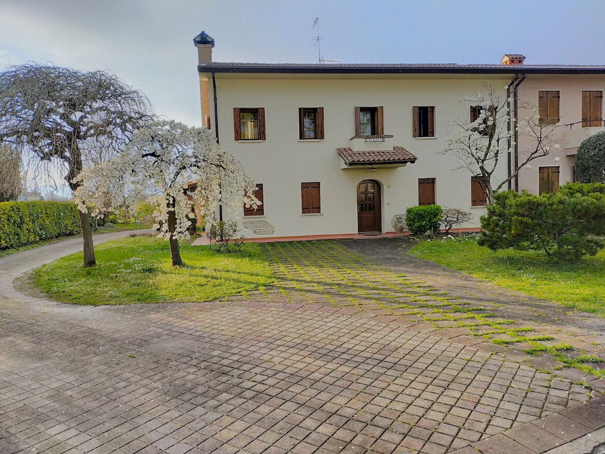 The image showcases a two-story building surrounded by a well-maintained garden. Green grass and blooming trees are evident in the foreground, while a winding pathway leads to the entrance. The exterior features several windows that invite natural light.