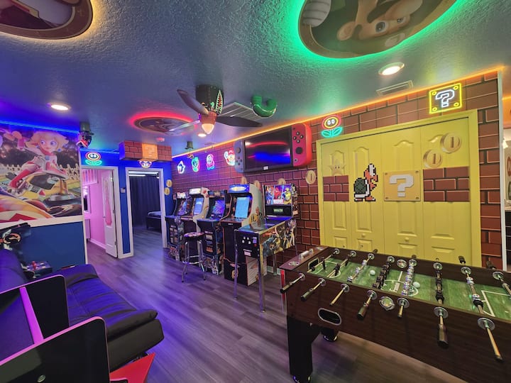 Rritu në një dhomë emocionuese lojërash Super Mario! Kjo hapësirë përmban makina arcade, një tavolinë futbolli, art muri me tematikë, drita neoni, një televizor të madh, dekor argëtues dhe një atmosferë të gjallë lojërash — të përsosura për një aventurë gjithëpërfshirëse në Mbretërinë e Kërpudhave me argëtim