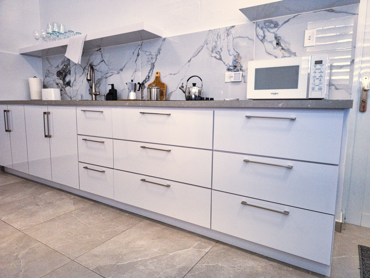 A modern kitchen features sleek white cabinetry with multiple drawers and a spacious countertop. A marble backsplash adds elegance, while a microwave and other appliances are readily available. Various cooking tools and a coffee maker are neatly arranged, emphasizing the kitchen's functionality.