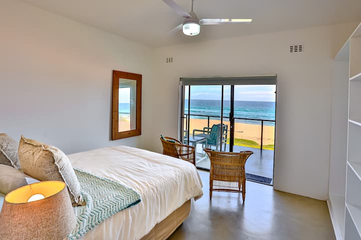 غرفة نوم بحجم كوين في شقة بالم بريز في الطابق الأرضي من البيت الرئيسي مع إطلالات رائعة على المحيط.