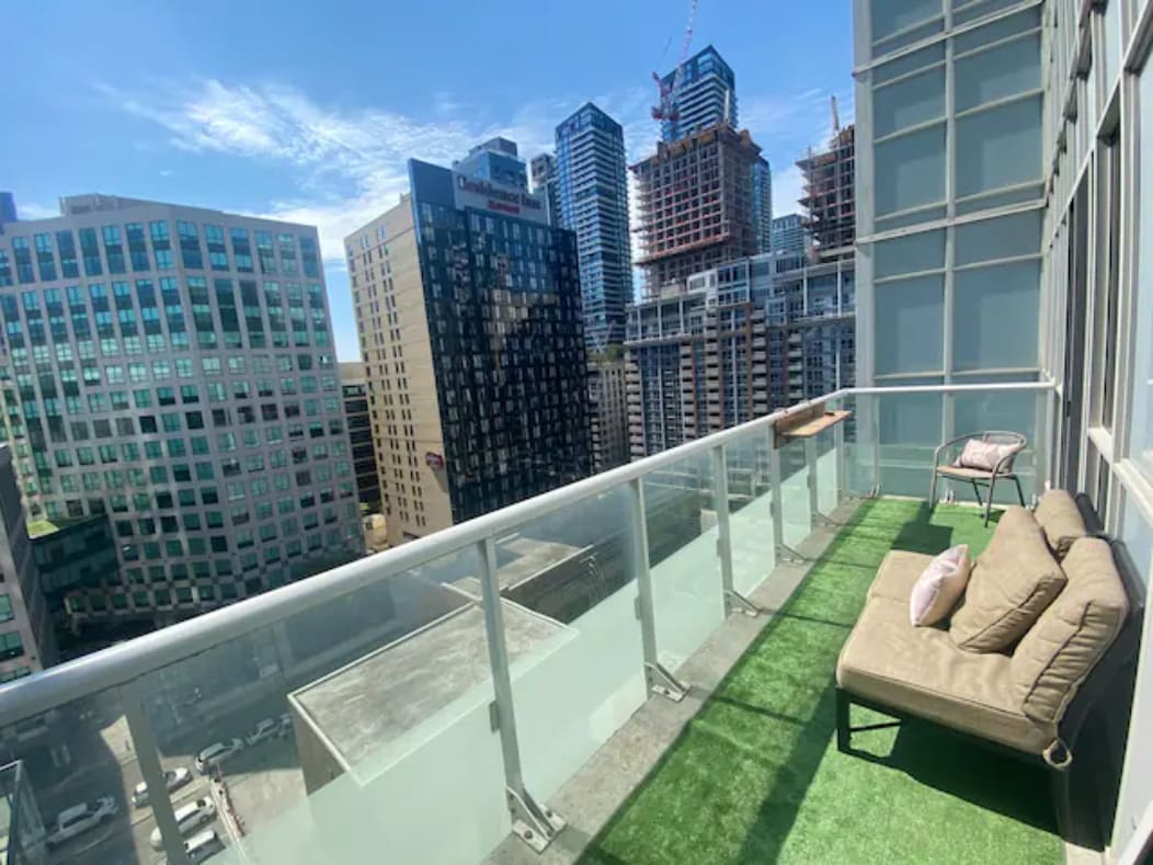A private patio is showcased with a view of the city skyline. It features a green lawn area and a cozy seating arrangement, providing a serene spot to relax while overlooking the bustling surroundings.