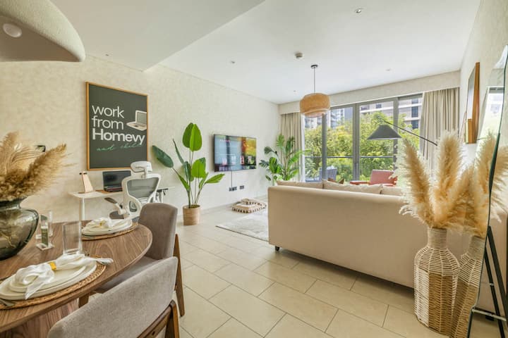 Кауч, телевизор, биро и трпезариска маса покрај прозорците.