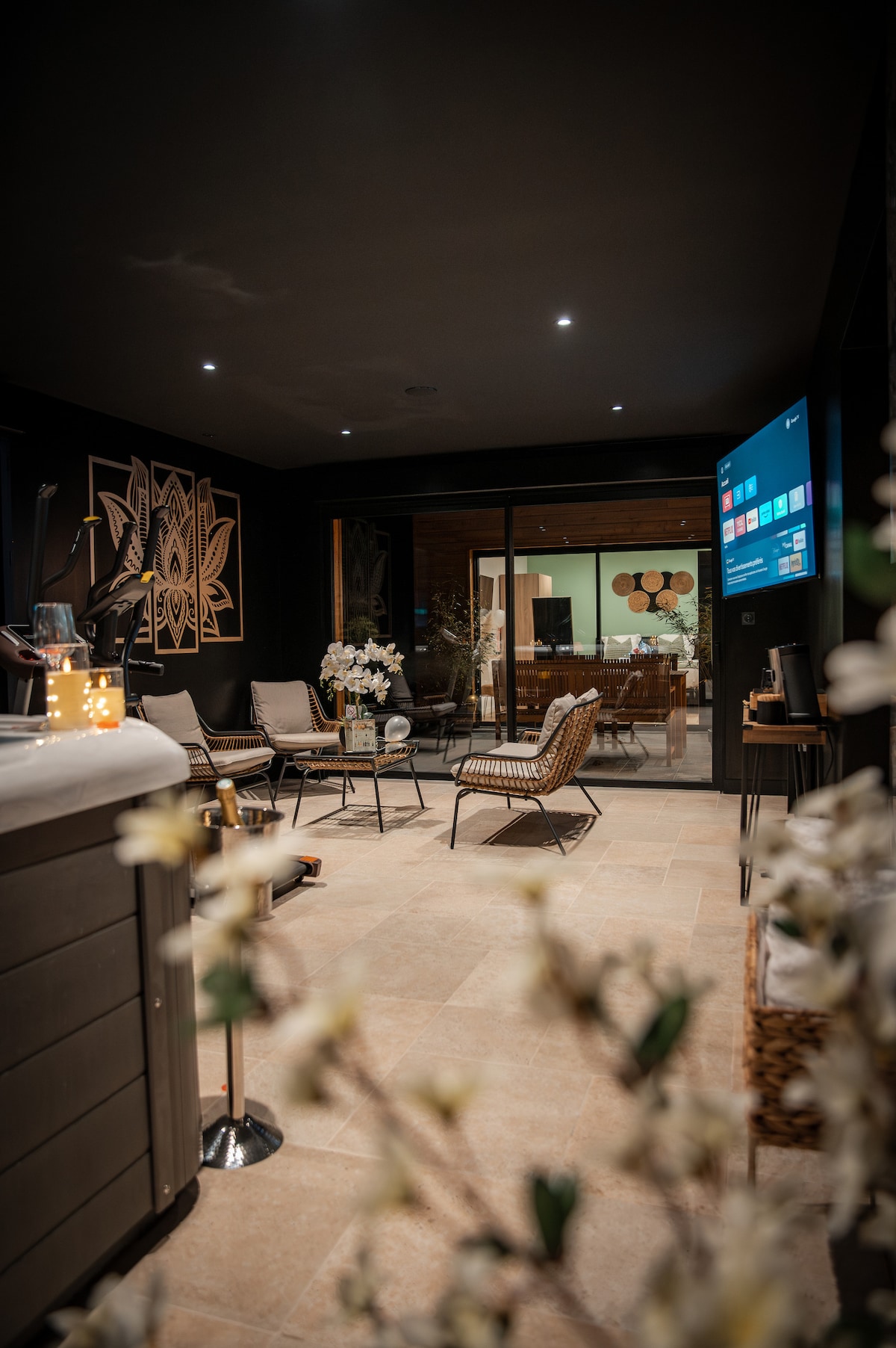 The interior space features a relaxed atmosphere with comfortable seating arrangements, including a modern chair and lounge chairs. A glass wall invites natural light and offers a view into the adjoining area. Decorative elements enhance the aesthetic appeal of the space.