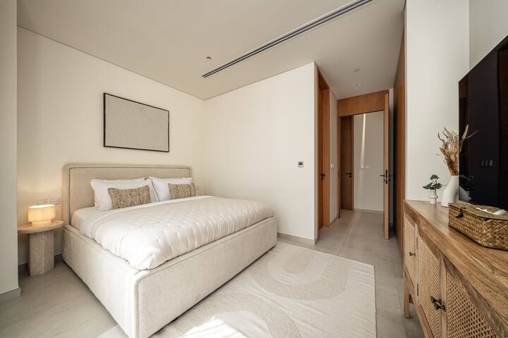 Una habitación tranquila y luminosa con una cama lujosa, muebles modernos y ventanas del piso al techo que ofrecen vistas panorámicas.