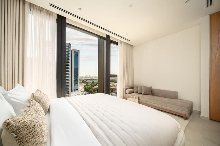 Una habitación tranquila y luminosa con una cama lujosa, muebles modernos y ventanas del piso al techo que ofrecen vistas panorámicas.