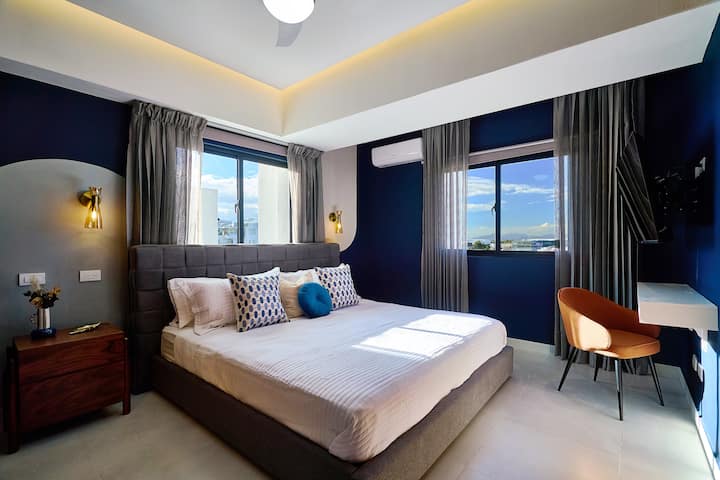 Úžasná hlavná spálňa má luxusnú posteľ veľkosti King, luxusný matrac, klimatizáciu, stropný ventilátor, zatemňovacie závesy, okolité svetlá, priestrannú skriňu, inteligentnú televíziu, písací stôl, krásny výhľad na mesto a luxusnú vlastnú kúpeľňu s dažďovou sprchou.