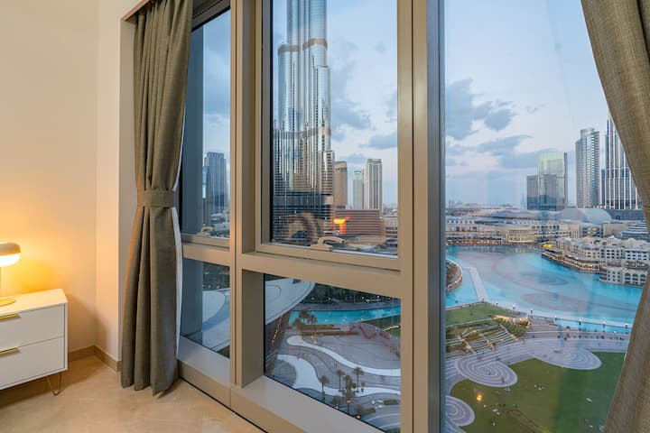 Модерна спална соба со син кадифен кревет, неутрален декор и елегантни вградени гардеробери.