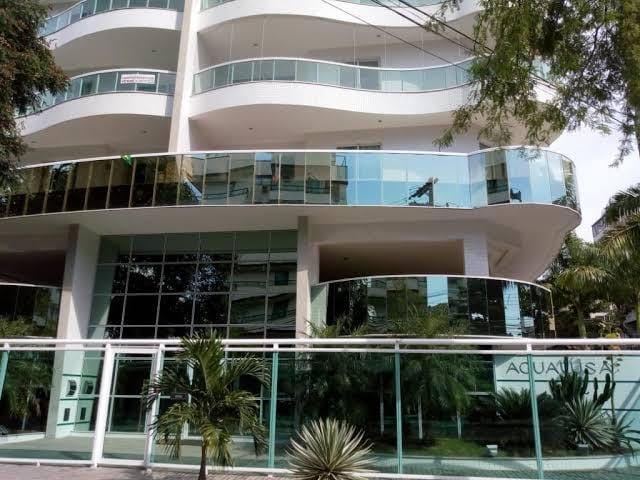 The building features modern architecture with expansive glass windows and balconies. A palm-lined walkway is visible in the foreground, leading to the entrance. The use of glass enhances natural light and offers a view of the surroundings.