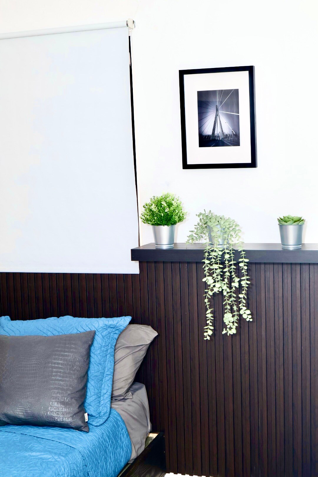 Chumba cha kulala chenye mwangaza na starehe kilicho na kitanda chenye rangi ya bluu, mito laini ya kijivu na blanketi lenye joto. Taa ya kisasa ya sakafu, kinara cha mbao cha kijijini na miguso ya kijani huunda sehemu ya kupumzika, maridadi inayofaa kwa ajili ya kupumzika.