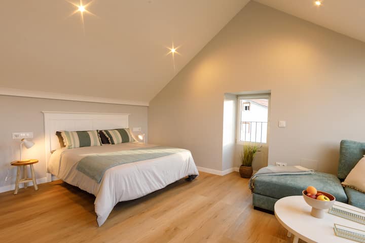 Acogedor dormitorio con cama de matrimonio, mesillas y luz ambiental desde elegantes focos en el techo. Un espacio diáfano y sereno, con una encantadora ventanita que aporta calidez y luz natural. Ideal para el descanso.