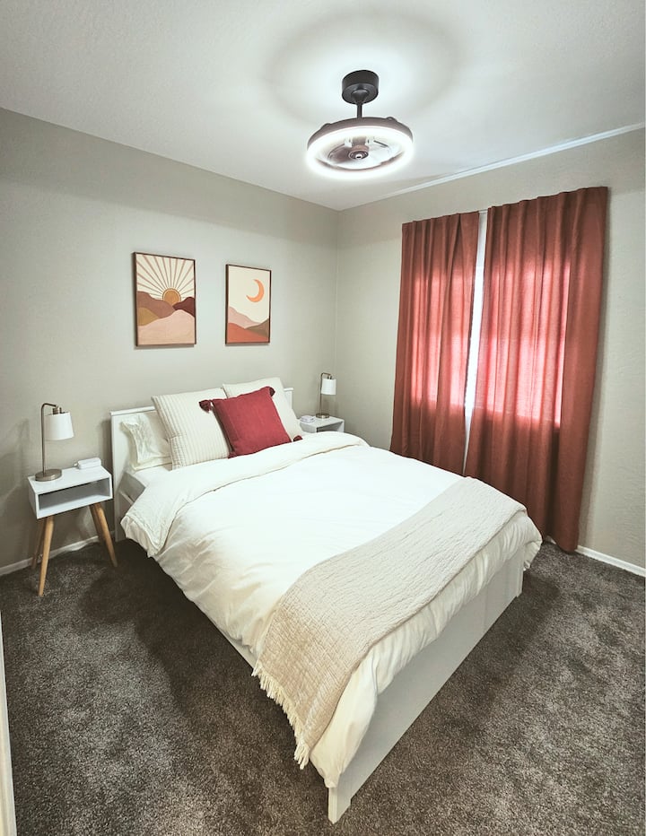 Manželská posteľ, stropný ventilátor a zatemňovacie závesy v miestnosti. 