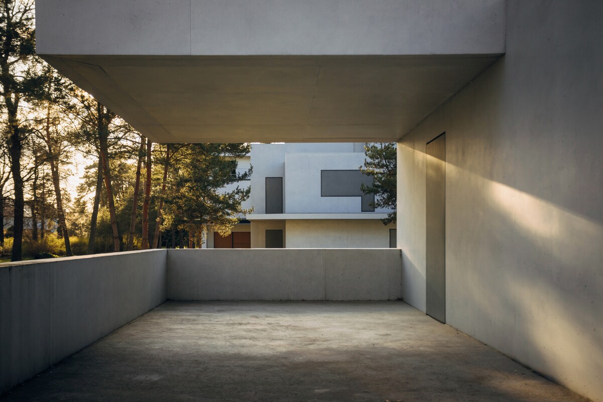 A spacious terrace is presented, framed by sleek concrete walls, allowing for an unobstructed view of the surrounding greenery. Soft sunlight filters through, creating a warm ambiance on the floor. The modern architectural lines suggest an integration of indoor and outdoor living.