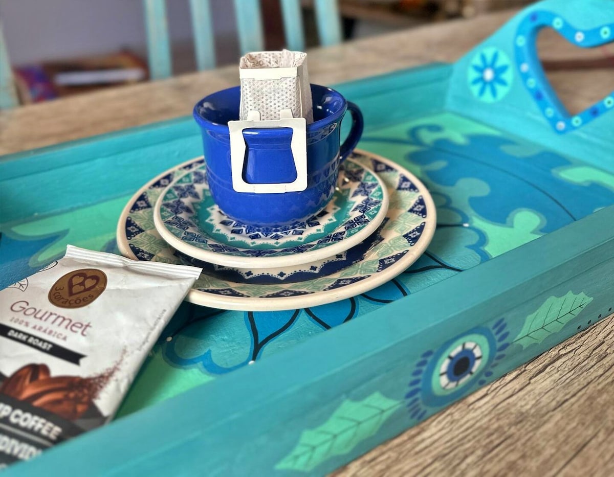 A vibrant serving tray features a blue cup with a sugar packet, placed atop decorative plates. A coffee packet rests beside the cup, showcasing a mix of artistic patterns and colors that enhance the overall presentation.