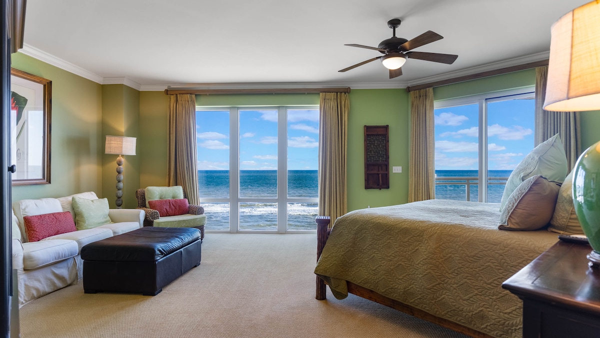 غرفة نوم 1 مع نافذة ممتدة من الأرض إلى السقف تطل على المحيط والشاطئ.