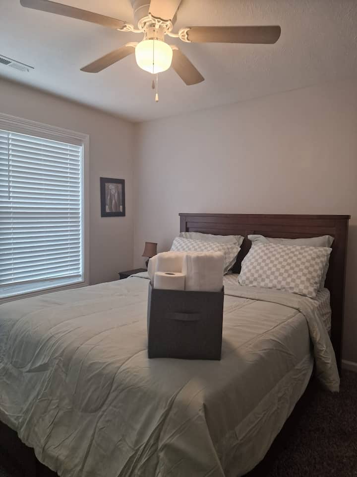 Acogedor dormitorio de invitados con una cama tamaño queen, lujosas sábanas, un ventilador de techo y una canasta de bienvenida con toallas limpias.