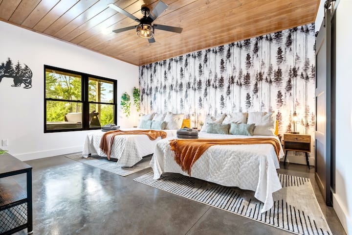 חדר קווין זוגי בקומה התחתונה, עם מבטא קיר יער, טלוויזיה עם מסך גדול, שולחנות צדדיים עם יציאות טעינה נוחות וארון לאחסון בגדים. 