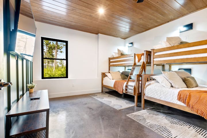 חדר קומתיים בקומה התחתונה עם 3 מיטות זוגיות מעל מיטות קומתיים מלאות. מקום נהדר לכל הילדים לישון בו, ממש ליד חדר המשחקים. טלוויזיה עם מסך גדול להזרמת המועדפים שלכם. לכל אזור קומתיים יש מנורה מותאמת אישית, יציאות טעינה ומדף לנוחיותכם.